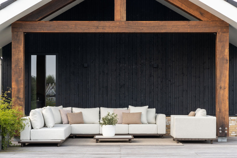 White outdoor sofa set on a patio with wooden pergola and black wall background