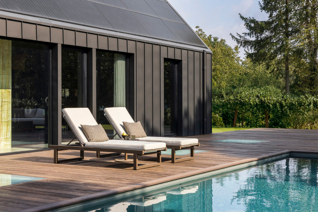 Two lounge chairs by a poolside with a modern house in the background
