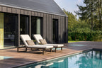 Two lounge chairs by a poolside with a modern house in the background
