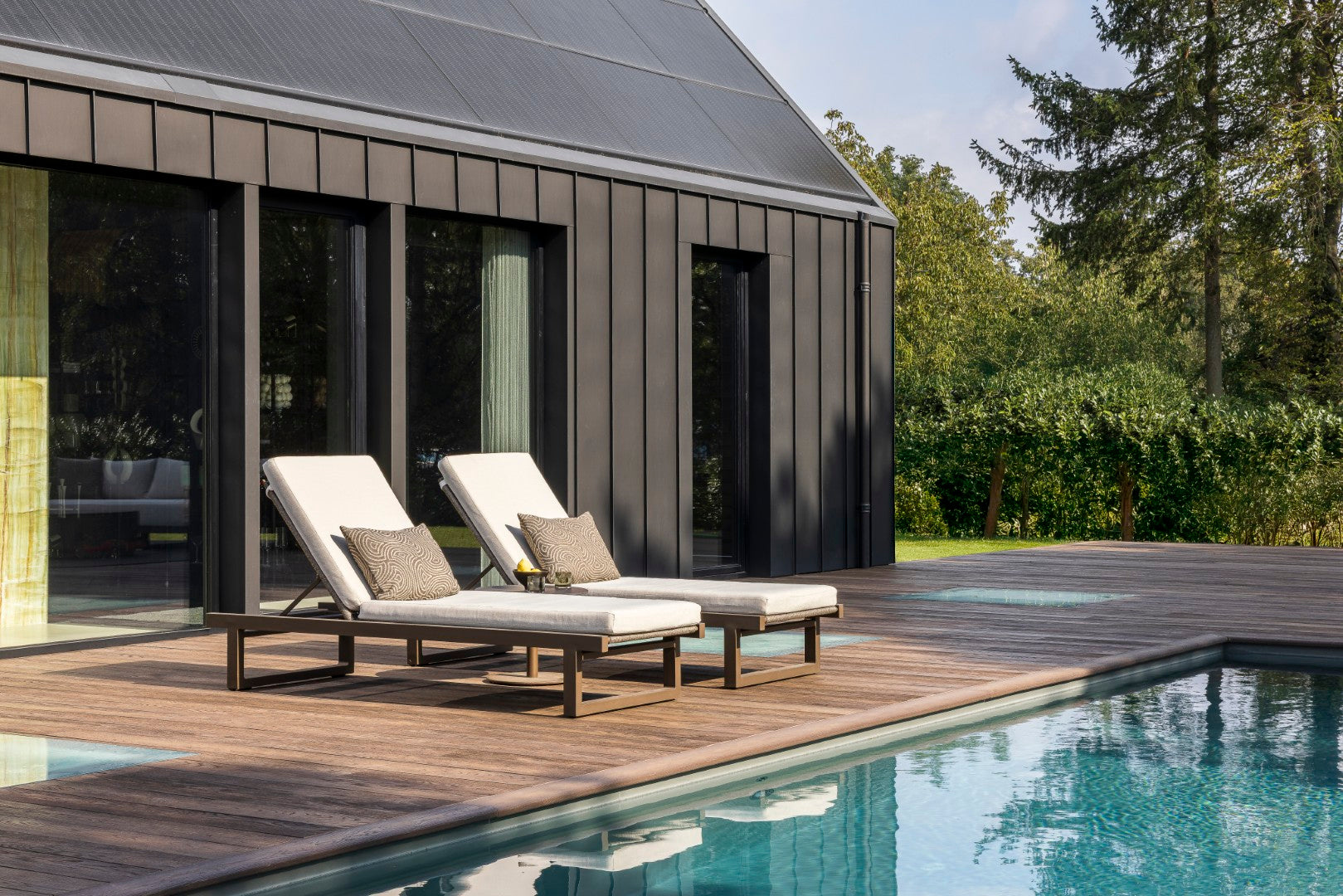 Two lounge chairs by a poolside with a modern house in the background