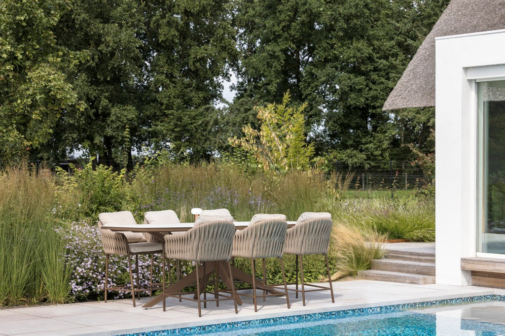 Outdoor dining area with chairs by a poolside, surrounded by greenery.