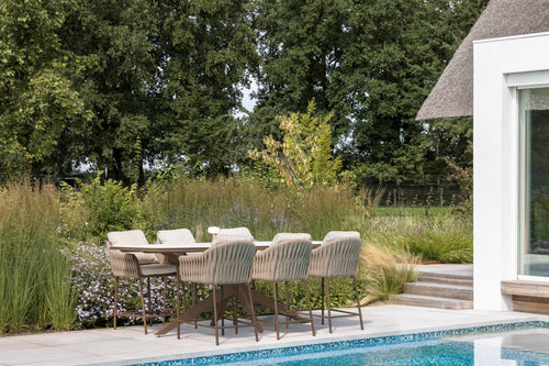 Outdoor dining area with chairs by a poolside, surrounded by greenery.