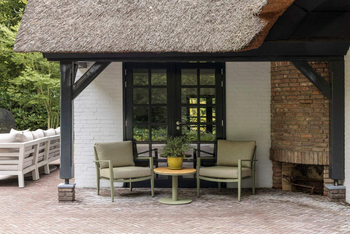 A cozy outdoor seating area features two olive-green casual dining chairs with cushioned seats, positioned around a round wooden side table.