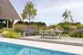 Outdoor dining area with table and chairs near a pool, surrounded by greenery and flowers.