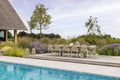 Outdoor dining area with table and chairs by a poolside, surrounded by nature.