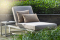 Outdoor lounge chair with cushions on a wooden deck surrounded by greenery