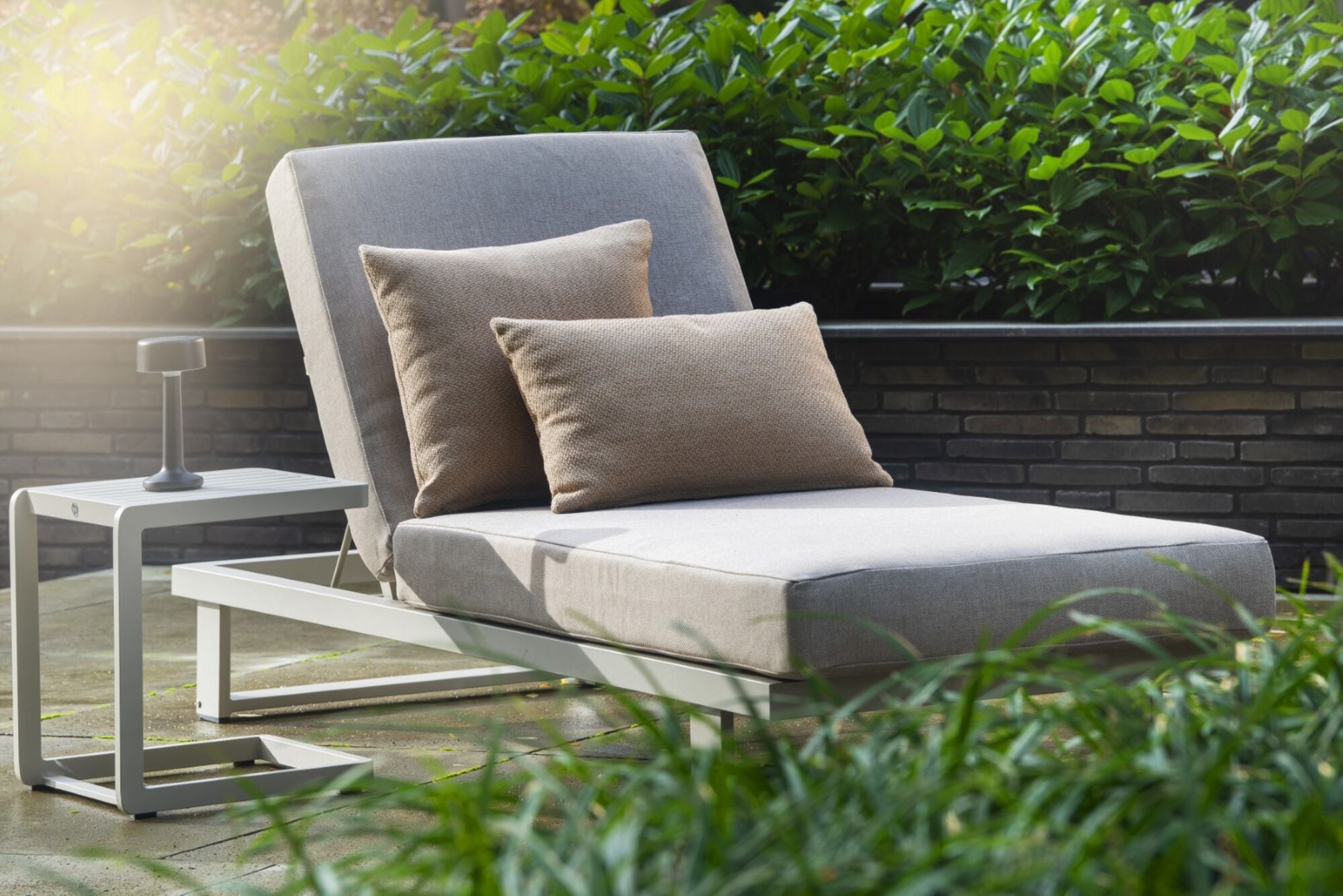 Outdoor lounge chair with cushions on a wooden deck surrounded by greenery