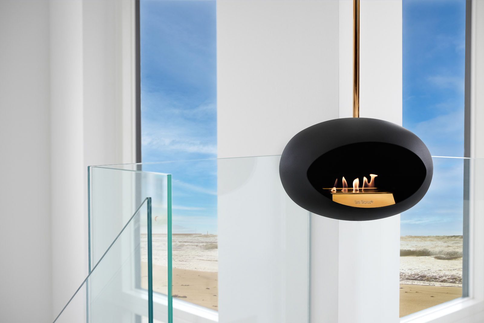 Modern black fireplace insert with glass door in a room with large windows overlooking a beach.