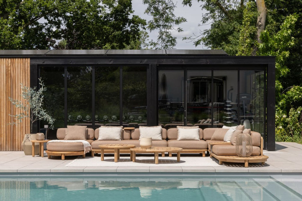 Outdoor patio area with a sectional sofa by a pool, surrounded by greenery.